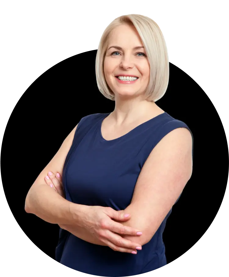 A middle-aged woman with light skin and short blonde hair, wearing a navy blue sleeveless top. She is smiling confidently with her arms crossed.