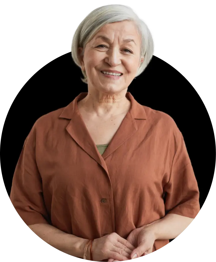 An elderly woman with light skin and short gray hair, wearing a brown blouse. She is smiling warmly.